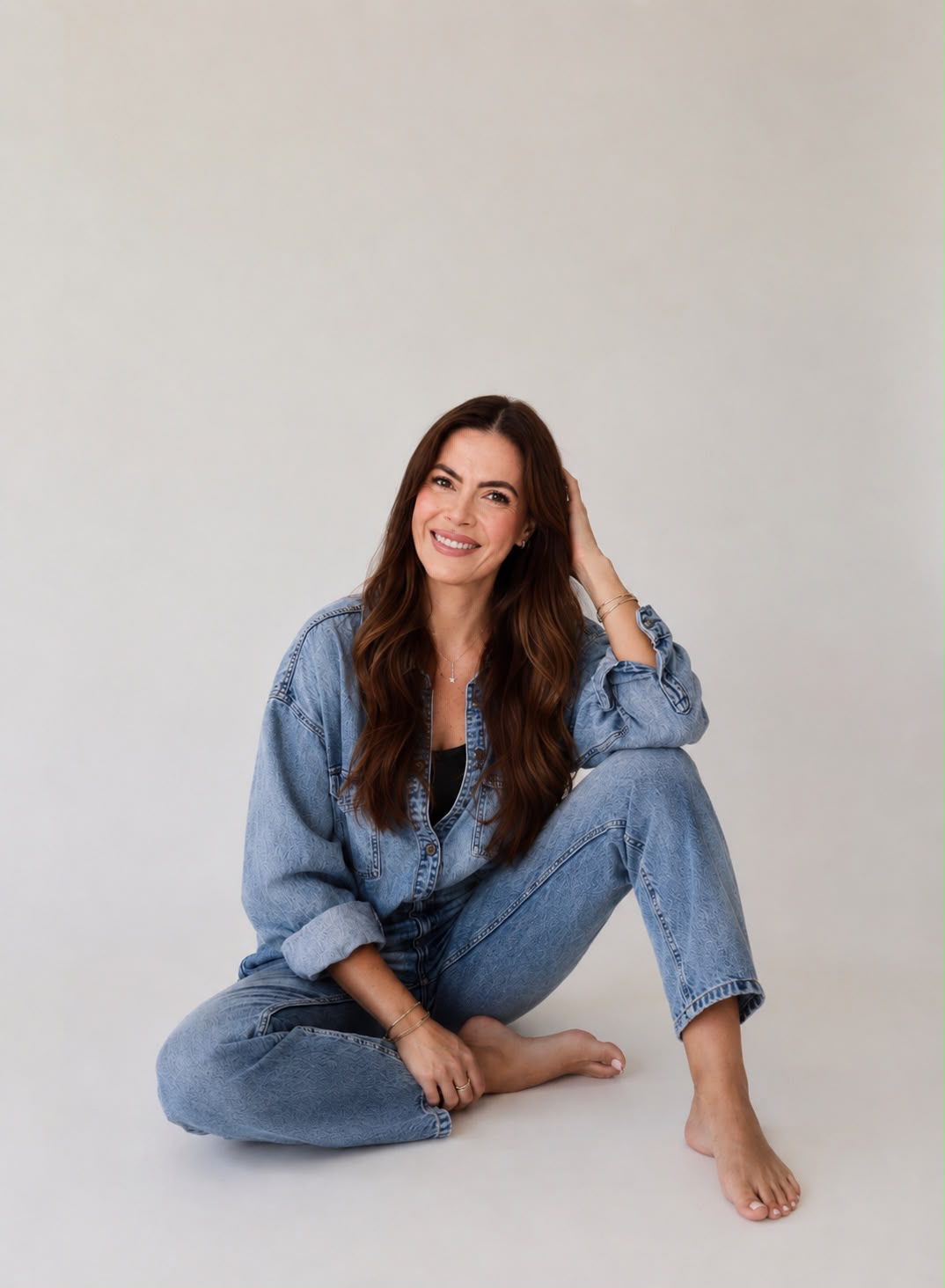 Erika Mello sorrindo, sentada no chão com roupa jeans